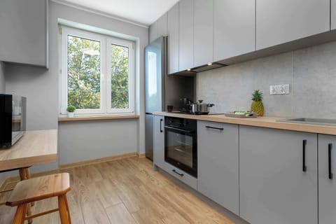 A modern kitchen with gray cabinets and built-in appliances. A small wooden stool adds a touch of warmth.