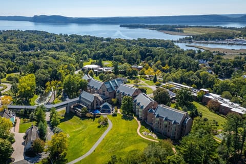 A panoramic aerial view reveals the expansive grounds of Windrose on Hudson, nestled among lush greenery with the serene Hudson River creating a breathtaking backdrop.