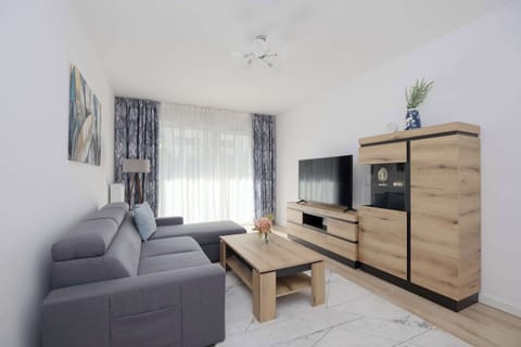 A cozy living room with a sofa, TV stand, and decorative painting on the wall. Natural light brightens up the neutral-colored space.