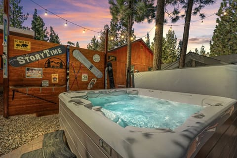 Soak in the private hot tub under string lights, surrounded by tall pines at dusk.