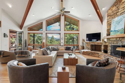 The heart of the home — a bright and inviting great room with soaring ceilings, a cozy stone fireplace, and large windows framing beautiful mountain views. A perfect space to relax, share stories, or unwind after a day exploring Durango.