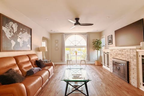 Bright, airy living room with a large arched window, cozy leather sofa, luxurious frame tv and fireplace. Enjoy morning coffee at the bistro table or relax in a warm, thoughtfully styled space with wood floors and natural light.