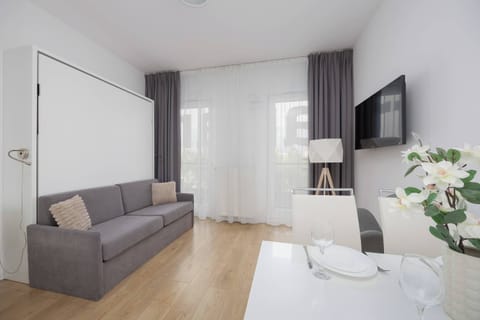 The bright living room with a large window and a comfortable sofa invites you to relax after a busy day, creating a cozy space to unwind.