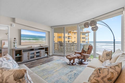 Enjoy ocean views from this cozy beachside living room featuring plush seating, a large TV, and access to a private balcony—perfect for relaxing after a fun-filled day at the shore.