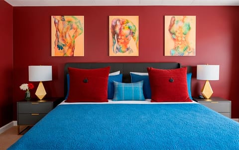 Stylish sleeping area in The Red Room, featuring a queen bed, rich red tones, modern artwork, and layered textures for a refined boutique feel.