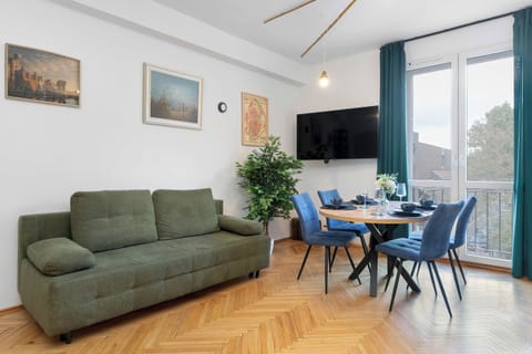 A cozy lounge with a comfortable sofa, TV, and dining table, filled with natural light from large windows.