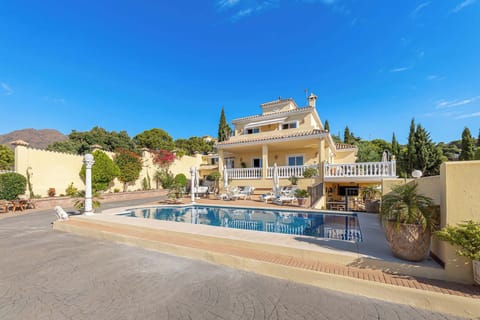 A beautiful villa with a swimming pool and manicured landscaping stands under a clear blue sky.