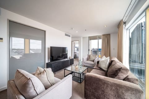 Unwind in the sunlit living area, complete with plush seating, smart TV, calming tones and balcony access—perfect for a quiet evening above the city buzz.