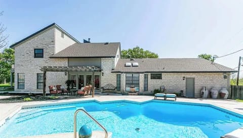 Backyard Poolside – A spacious view of the pool area showing the home’s rear stone exterior, pergola-covered patio seating, and large windows that open to the backyard.