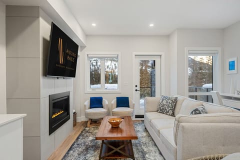 Main floor living room with a cozy, gas-lit fireplace, comfortable seating options and walkout access to the hot tub/balcony.
