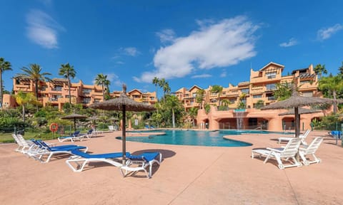 Lounge chairs line a pool deck under a sunny sky, offering a relaxing view of the pool and distant scenery.