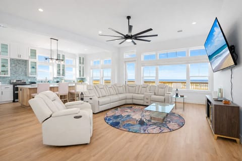 Bright open-concept living room with large windows, coastal decor reclining sectional seating, and marsh views in this Galveston vacation rental.
