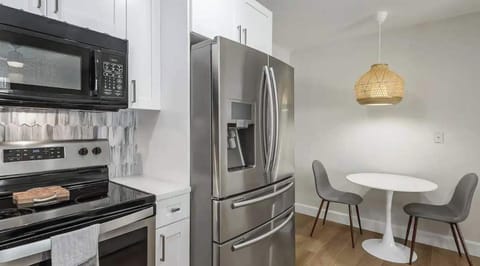 Modern kitchen and dining nook featuring stainless steel appliances, sleek white cabinetry, and a cozy two-seat table under a woven pendant light—perfect for enjoying meals in a bright, inviting space.