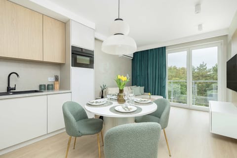 Contemporary living room with teal curtains, minimalist furniture, and warm wood flooring. The layout emphasizes comfort and brightness.