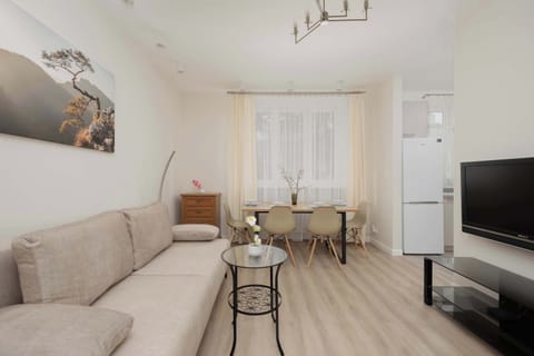 A cozy living room featuring a beige sofa, wooden coffee table, and TV. Light-colored walls and flooring create a bright and inviting space.