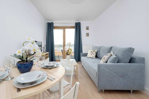 A bright living room with a comfortable sofa and a dining table set for a meal invites you to enjoy time together in the natural light streaming through the large window.