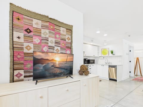 Bright, open living area with vibrant wall art, 32" smart TV, and modern kitchen