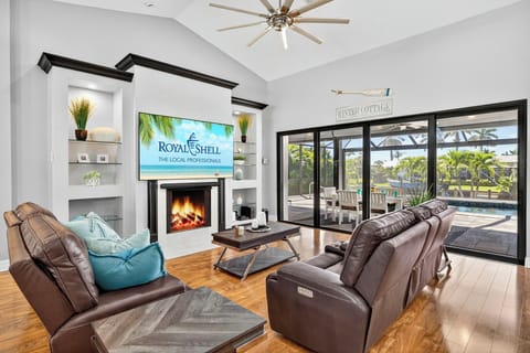 Open-concept living area featuring cozy leather seating, a sleek fireplace, and sliding glass doors leading to the pool and outdoor dining area — perfect for relaxing or entertaining.