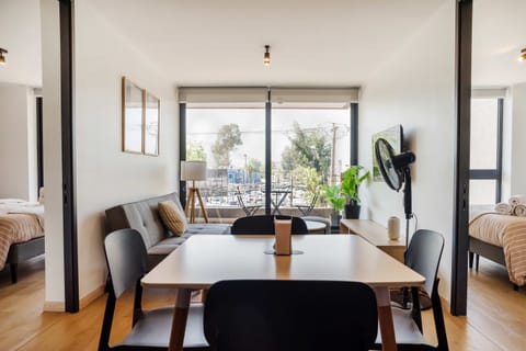 Bright and modern living area with a cozy sofa, dining space, and a view of lush greenery through large windows.