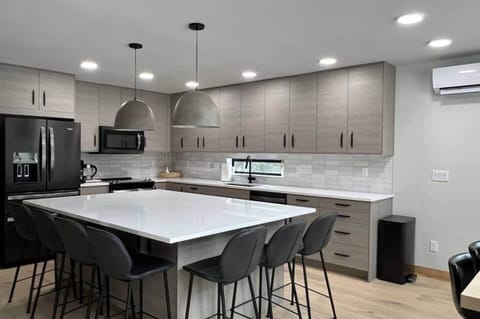 Enjoy the fully stocked, spacious kitchen: modern gray cabinetry, a large white island with ample seating, and sleek appliances, this area is perfect for cooking and gathering. Warm wooden floors and stylish pendant lights add a touch of elegance. 