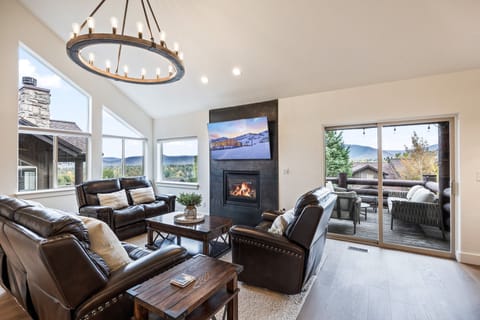 A bright, open-concept living area featuring large windows that frame stunning mountain views. Cozy leather seating, a modern stone fireplace, and warm natural light create the perfect retreat for relaxation and gathering.