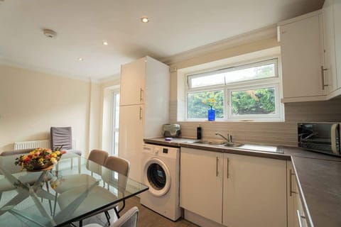 Bright kitchen with modern appliances, a glass dining table, and large windows offering garden views.