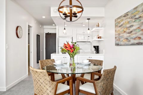   Gather around a glass-topped table framed by woven chairs, soft coastal tones, and warm globe pendant lighting   WH1-1218