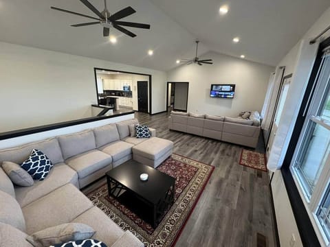 The living room features an LG 55" smart tv, 2 ceiling fans, two large sectional couches with rugs and coffee tables with drink coasters, and ample lighting.