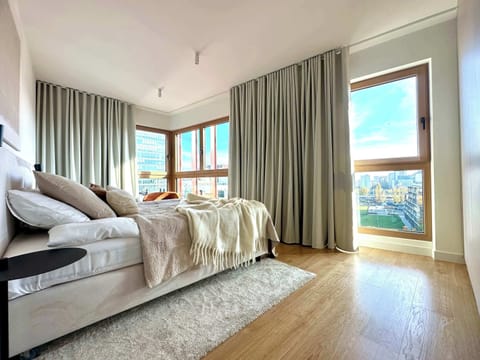 Soft fabrics and bright tones in the bedroom create a serene atmosphere, while large windows let in the morning light and open up to a city view.