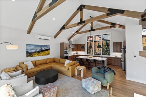 The open concept living area offers ample seating, air conditioning, cozy fireplace, a mounted TV, and a vaulted ceiling.