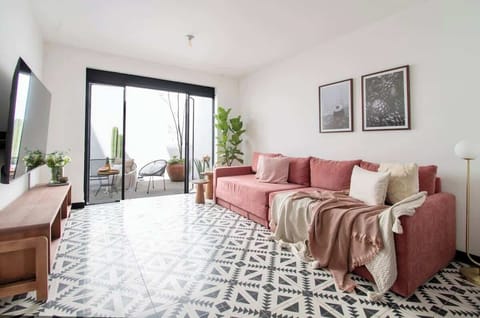An airy living room filled with natural light, where a terracotta sofa and patterned floors set a modern, inviting tone. The doors open to the terrace, blending indoor comfort with an effortless outdoor charm.