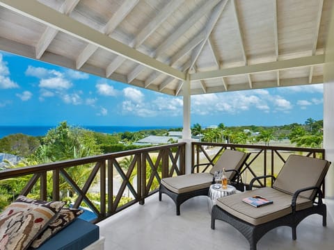 Balcony with lounge chairs, ocean views, tropical greenery, and vaulted ceiling