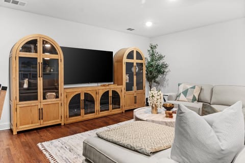 Relax in the cozy living area with oversized seating and a large smart TV — a comfortable spot for movie nights after exploring nearby Korean BBQ spots in Carrollton, Addison’s restaurant scene, or shopping at Valley View Center redevelopment area.