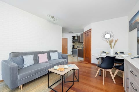 A cozy living room with a gray couch and soft pastel cushions. The minimalist design and wooden floor add warmth and comfort.