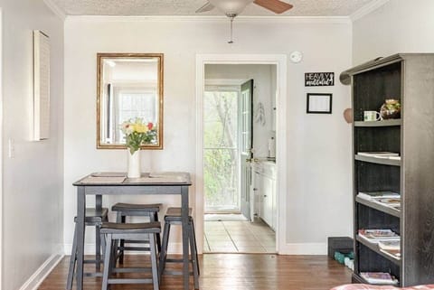 A quaint dining area with a small breakfast nook, fresh flowers, and a mirror reflecting natural light. The nearby bookshelf and hardwood floors add charm, while the open view to the back entryway creates a bright, airy feel for your stay.