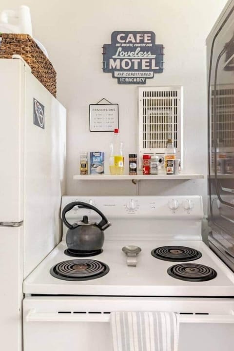 A charming kitchen with a tea kettle on the stovetop, a shelf stocked with spices, and retro Nashville decor. A conversion chart and fridge magnets add character to this functional cooking area.