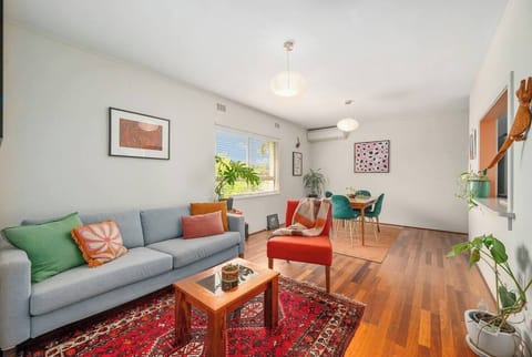 Styled with mid-century warmth, the living area features a soft grey sofa, deep red rug, and curated art—an inviting space to unwind in comfort after exploring Fremantle.