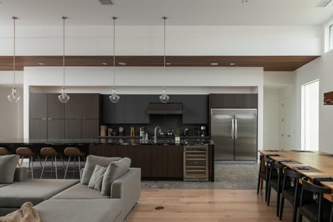 A fully equipped chef's kitchen featuring sleek, dark cabinetry, stainless steel appliances, and a wine cooler.