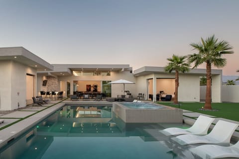 The ultimate outdoor entertainment space at dusk, featuring the illuminated pool, hot tub, outdoor bar, and multiple seating areas.