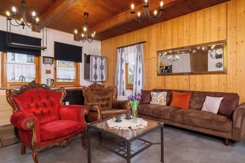 A cozy living room with wooden walls and a beamed ceiling, featuring red and brown sofas arranged around a coffee table. Warm lighting enhances the rustic mountain atmosphere.