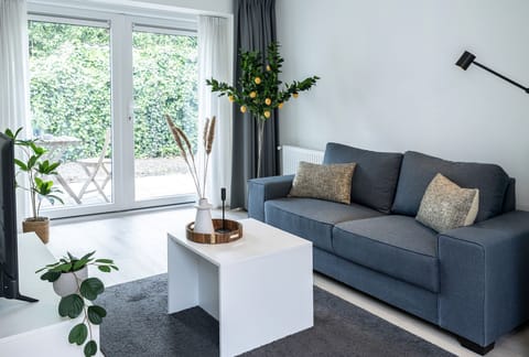 Bright living room with a comfy blue sofa, lemon tree decor, and large garden doors that fill the space with light. Stylish and peaceful atmosphere.