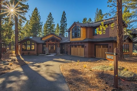 Modern mountain lodge nestled among towering pines with elegant stone and wood architecture featuring spacious garage and natural landscaping.