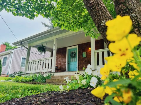 Charming cottage with a teal door, cozy porch swing, and vibrant garden blooms.