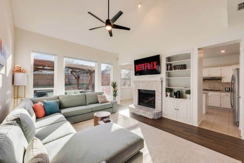 This bright, stylish living room features a plush sectional sofa, colorful throw pillows, 58” Smart TV, & a decorative fireplace for added charm. Large windows fill the space w/ natural light & offer pool views. Perfect for relaxing or entertaining!