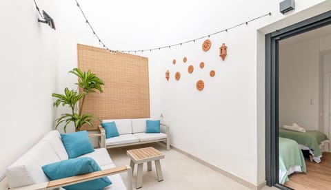 Private terrace with outdoor seating area featuring white cushioned benches with teal blue accent pillows. Bamboo privacy screen, decorative ceramic wall tiles, string lighting, and potted plants create a cozy atmosphere.