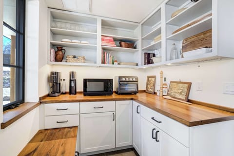 This bright prep area combines modern functionality with warm design touches. Wood countertops, open shelving, and sleek appliances make it a practical yet inviting corner of the home.