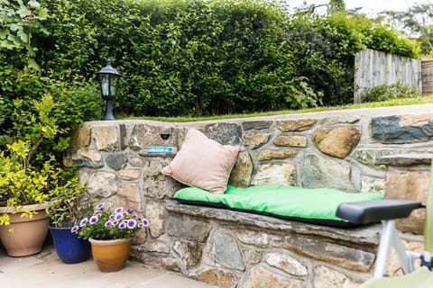 Patio seating area built within stone wall with cushions and a light and potted plants