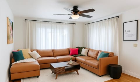 Bright, contemporary living room with large windows, soft white curtains, and a comfortable sectional – the perfect gathering space.