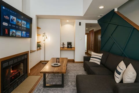 Loft living room with fireplace, big-screen smart TV, and bold teal geometric accent wall beneath the stairs.