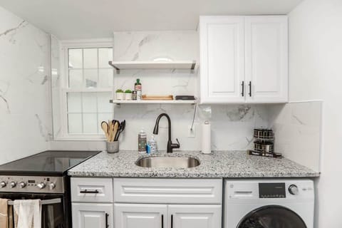 Kitchen with washer and dryer combo, stove, oven, coffee maker, and dish storage. 